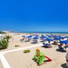 Spiaggia con ombrelloni blu e scivolo verde in primo piano.