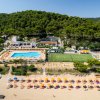 Resort sulla spiaggia con piscina, campo da tennis e lettini.
