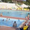 Persone giocano in due piscine adiacenti contornate da lettini gialli.