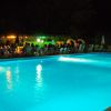 Piscina illuminata di notte con persone sedute a tavolini vicini.