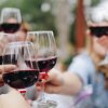 Persone brindano con bicchieri di vino rosso.