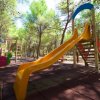 Scivolo giallo in un parco giochi tra alberi alti.