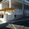 Una villa bianca con balconi e muretto sul davanti, situata su una strada in pendenza.