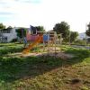 Un parco giochi con uno scivolo arancione su un prato. Sullo sfondo si vedono alberi e una casa.