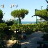 Giardino con panchine e palme, vista sul mare e bandiere sventolanti.