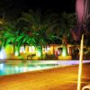 Piscina illuminata di notte, palme illuminate e ombrelloni chiusi.