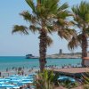 Spiaggia affollata con palme e torri sullo sfondo.