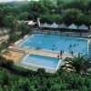 Piscina all'aperto con persone che nuotano, circondata da vegetazione.