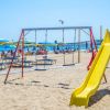 Parco giochi su una spiaggia con mare e ombrelloni.